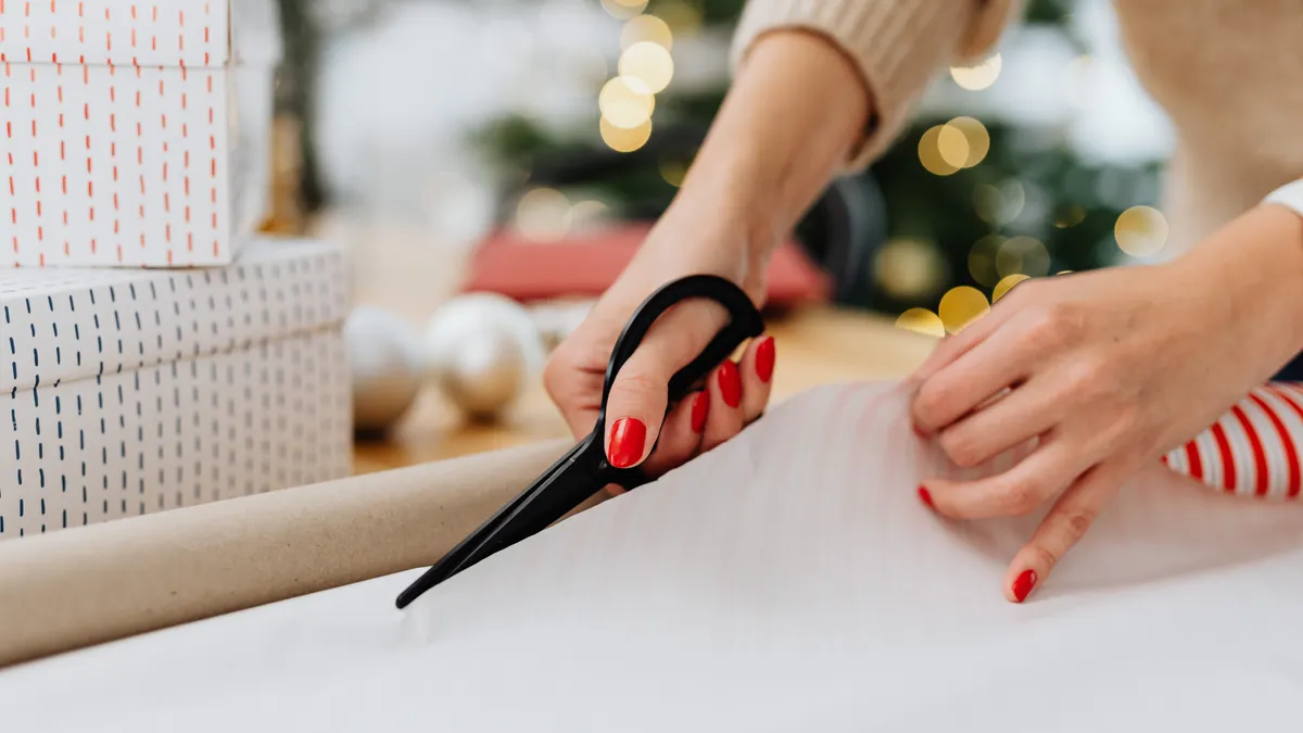 Hands cutting wrapping paper beside wrapped boxes