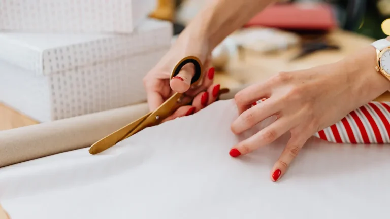 Hands cutting wrapping paper beside gift boxes