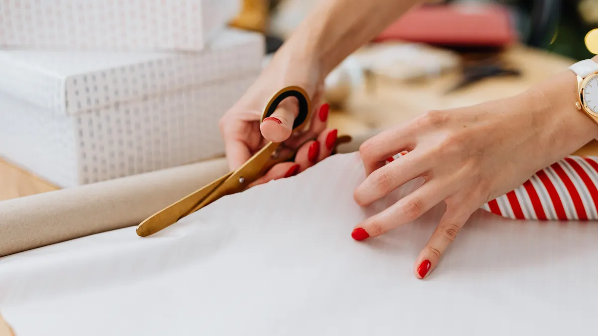 Hands cutting wrapping paper beside gift boxes