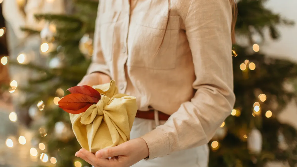 How to wrap a gift in fabric Person holding a yellow fabric-wrapped present