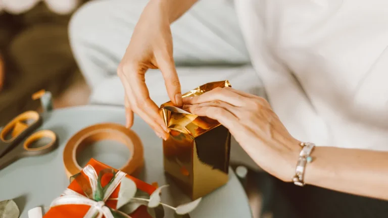Hands folding gold wrapping paper around a small gift box